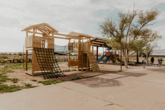 A playground and jungle gym behind a basketball court, children playing in the distance